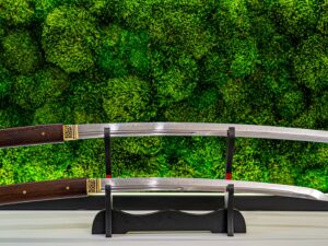 Zestaw Daisho Warszawa – katana z drewna różanego i wakizashi T10 z przedłużanymi rękojeściami na stojaku ekspozycyjnym na tle zielonego mchu.